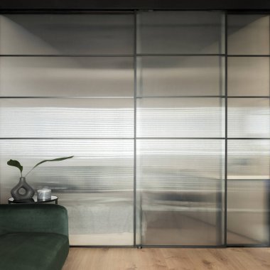 Tempered glass wall in modern room with green sofa, decorated side table and wooden floor