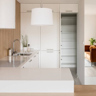 Modern kitchen with white furniture and lamp, mirror wall and open doors to pantry