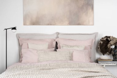 Charming bedroom with bright details, pink, gray and beige bedclothes on big bed, delicate art above bed and modern black lamp