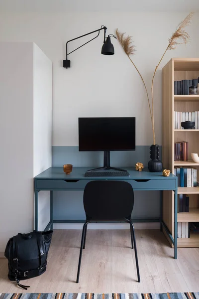 Stylish blue desk, books and decorations in simple study room with white walls and wooden floor