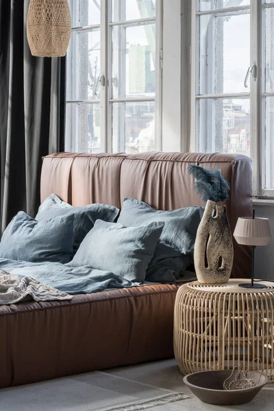 大而舒适的床 有皮革床头板和蓝色 亚麻床上用品和枕头在明亮的卧室与藤蔓床头柜和灯 — 图库照片