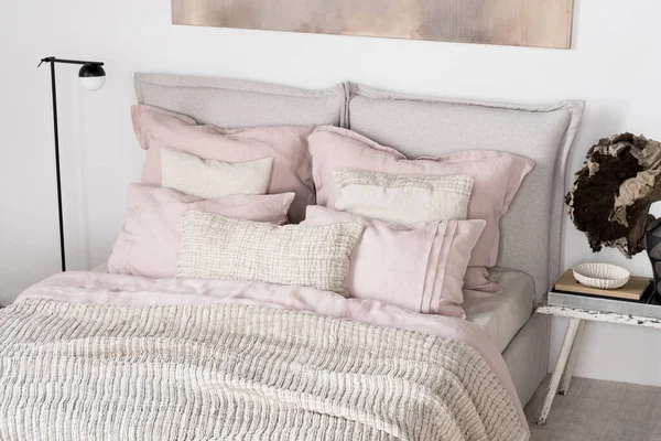 舒适的床 床旁边有时髦的粉色和米黄色的床上用品和枕头 还有现代的黑色灯和床头柜装饰 — 图库照片