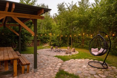 Kamp alanı ahşap bank ve bahçe çardağının altındaki masa, salıncak ve dekoratif ışıklar ormandaki kampta.