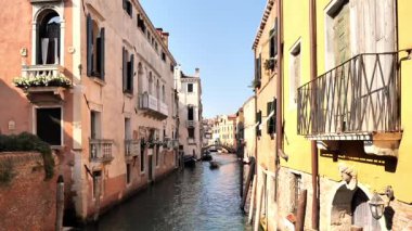 Eski binalar ve kırsal dokularla çevrili dar bir Venedik kanalında süzülen sürat teknesi. Uzak çan kulesi seyahat, şehir keşfi, denizcilik veya sinematik çekim için derinlik katar.