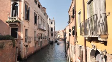 Eski binalar ve kırsal dokularla çevrili dar bir Venedik kanalında süzülen sürat teknesi. Uzak çan kulesi seyahat, şehir keşfi, denizcilik veya sinematik çekim için derinlik katar.