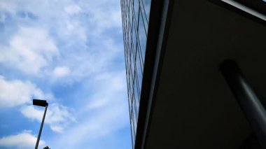 Mavi gökyüzünü ve bulutları yansıtan modern cam binanın alçak açılı görüntüsü. Geometrik çizgileri olan şık şehir mimarisi, gayrimenkul, şehir manzarası veya editör görüntüleri için ideal..