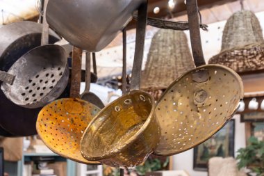 Antique copper spoons and kitchen utensils hanging in antique store clipart