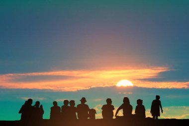 Siluet insanlar yerde oturuyor ve turuncu bulutlar gökyüzünde gün batımı ve kuşlar uçuyor, konsept aile partisi tatilde, hafta sonu dışarıda parti  