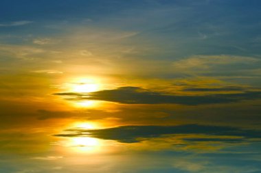 Günbatımını yansıtan koyu mavi turuncu gökyüzü ve koyu sarı bulut ve güneş sol alevin altında.