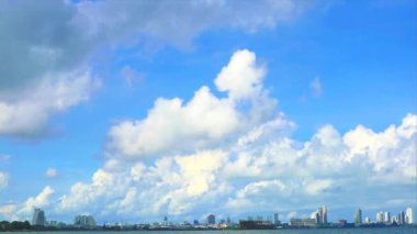 Güzel beyaz bulut mavi gökyüzü yağmur mevsiminde denizin ve şehrin inşaatının üzerinde yuvarlanıyor.