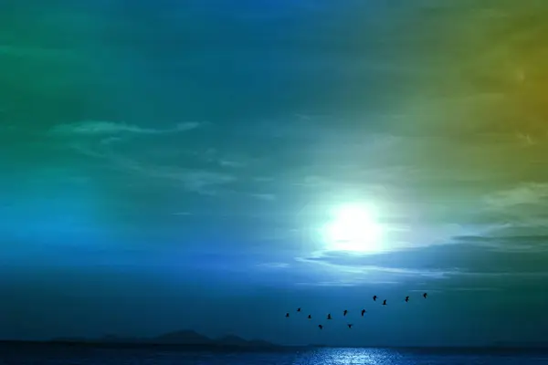 Full moon teal blue green cloud and silhouette birds flying pass over lake on night sky