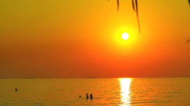 Nefes kesici bir günbatımı okyanusu aydınlatır, sıcak renkleri yansıtır. Siluetli figürler huzurlu atmosferin tadını çıkarırlar, bir huzur ve güzellik anı yakalarlar..
