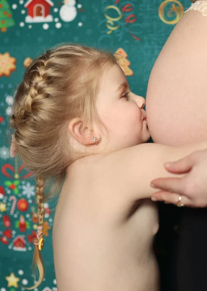 A little girl hugs her mother's stomach. Pregnant mother stands next to her daughter, big belly, term 7 months