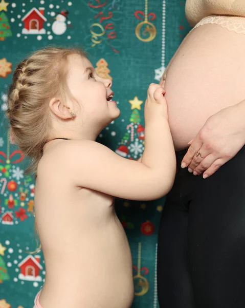 A little girl hugs her mother's stomach. Pregnant mother stands next to her daughter, big belly, term 7 months