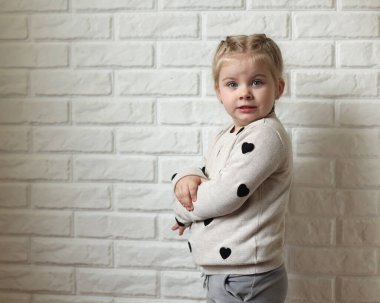 Funny child on a white brick background. A little girl poses in front of the camera