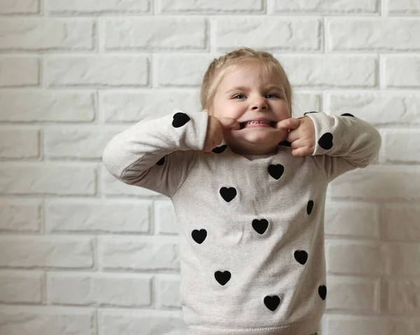 Funny child on a white brick background. A little girl poses in front of the camera