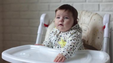 A little girl is sitting in a child's chair. The kid looks at everything with an interesting look