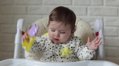 A little girl is sitting in a child's chair. The kid looks at everything with an interesting look