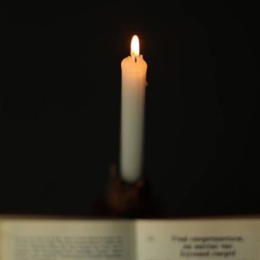 A candle and a book on the table. Bible for reading