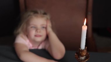 A small child makes a wish while looking at a candle. Dreams Come True