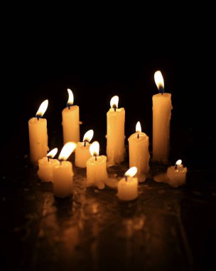 A few candles glow in the dark. Burning candles on a black background. Yellow candles. The flame burns out