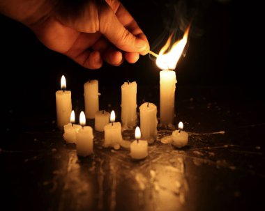 A few candles glow in the dark. Burning candles on a black background. Yellow candles. The flame burns out
