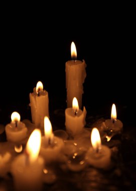 A few candles glow in the dark. Burning candles on a black background. Yellow candles. The flame burns out
