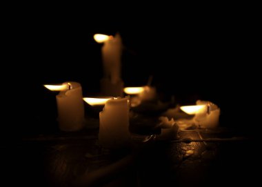 A few candles glow in the dark. Burning candles on a black background. Yellow candles. The flame burns out