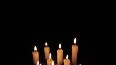A few candles glow in the dark. Burning candles on a black background. Yellow candles. The flame burns out