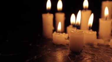A few candles glow in the dark. Burning candles on a black background. Yellow candles. The flame burns out