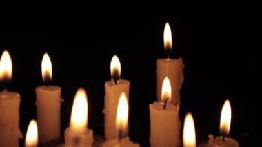 A few candles glow in the dark. Burning candles on a black background. Yellow candles. The flame burns out