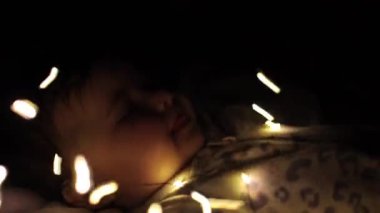 A little girl is playing with garlands. The lights shine in the dark, the child is interested in it