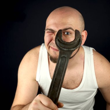 The plumber gets to work. He has a very large wrench. A man with a beard