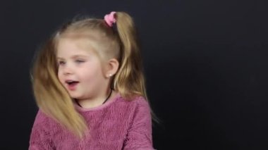 A little girl on a black background, she is dancing funny and has a funny expression on her face