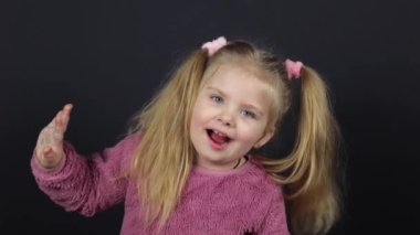 A little girl on a black background, she is dancing funny and has a funny expression on her face
