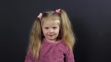 A little girl on a black background, she is dancing funny and has a funny expression on her face