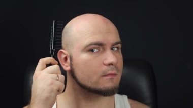 The bald man takes a comb and combs his head. Combing his bald head, A man without hair