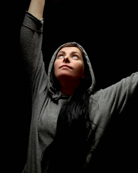 A girl in the dark, with her head covered. Black background behind the woman, a lamp shines on her from the side