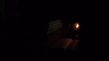 An ancient kerosene lamp, standing on the table, a book next to it, darkness around. Black background, light from a lamp