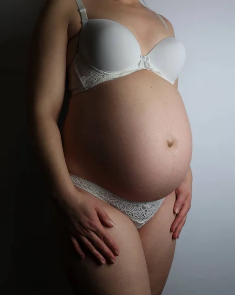 Pregnant woman in underwear. She is 30 weeks pregnant and has a big belly. Expecting a child. Third pregnancy. Pregnant girl. White background and linen