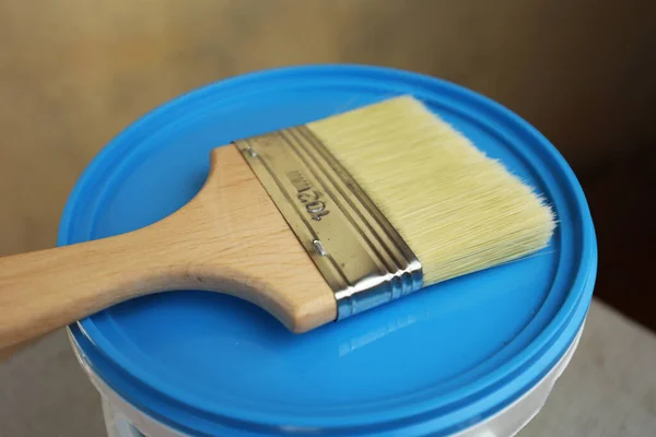 A bucket of white paint and a brush. Painting works in the premises. Tidying up the apartment. Repair of premises. A white bucket with a blue lid.