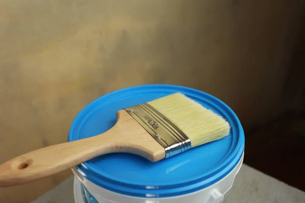 A bucket of white paint and a brush. Painting works in the premises. Tidying up the apartment. Repair of premises. A white bucket with a blue lid.