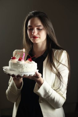 Elinde pasta olan güzel bir kız. Bu onun doğum günü. Beyaz pasta, stüdyo fotoğrafı. Doğum günü dileği tutuyorum. Mütevazı bir tatil