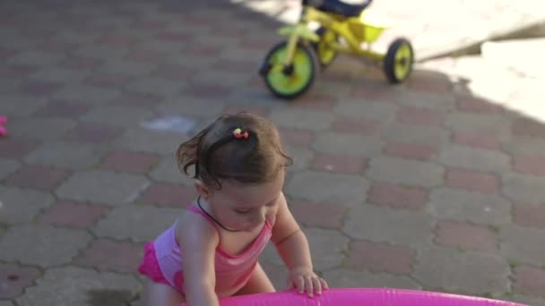 子供は子供のプールで遊びます 庭で泳ぐ 日陰に膨脹可能なプール 女の子は水 ピンクの膨脹可能なプールが大好きです 入浴のための温水 水着で幸せな子供 — ストック動画