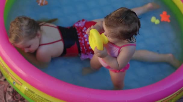 子供は子供のプールで遊びます 庭で泳ぐ 日陰に膨脹可能なプール 女の子は水 ピンクの膨脹可能なプールが大好きです 入浴のための温水 水着で幸せな子供 — ストック動画