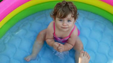 Havuzdaki çocuklar, yazın çok sıcak olur. Küçük bir kız. Çocuk havuzunda oynayan bir çocuk. Bahçede yüzmek, gölgede şişme havuz. Kız suya bayılıyor. Mayolu mutlu çocuk.
