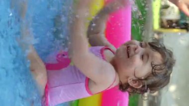 Havuzdaki çocuklar, yazın çok sıcak olur. Küçük bir kız. Çocuk havuzunda oynayan bir çocuk. Bahçede yüzmek, gölgede şişme havuz. Kız suya bayılıyor. Mayolu mutlu çocuk.
