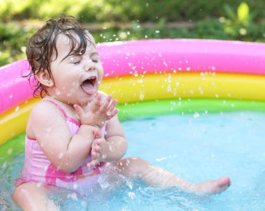 Havuzdaki çocuklar, yazın çok sıcak olur. Küçük bir kız. Çocuk havuzunda oynayan bir çocuk. Bahçede yüzmek, gölgede şişme havuz. Kız suya bayılıyor. Mayolu mutlu çocuk.