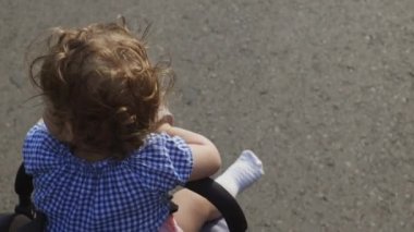 Bebek arabasında bir çocuk. Bir kız beşikte oturuyor, annesi el arabasını itiyor. Bebekle birlikte temiz havada bir yürüyüş. Gri bebek arabası, annelik, çocuk bakımı.