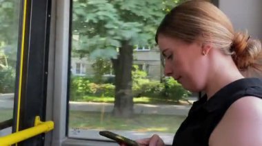 Kız otobüste oturuyor ve ata biniyor. Elinde telefon var. İnterneti kullanırken haber akışına bakıyorum. Şehir manzarası, toplu taşıma, pencerenin yanındaki kadın. İşe otobüsle gider.